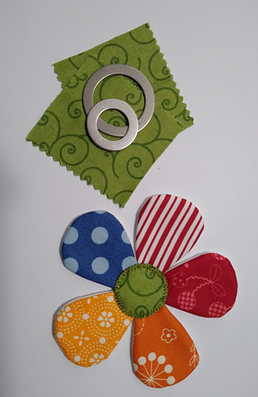 Green fabric squares, applipop round templates, colorful fabric flower with green applipop circle in the middle