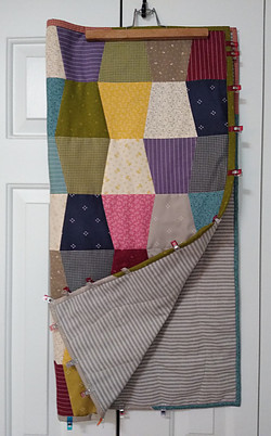 Small quilt made from multi colored scraps of fabric.  Quilt clips used to hold binding in place until stitched in place