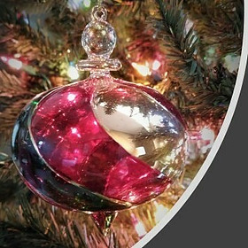 red and gold glass Christmas ornament hanging from a lighted Christmas tree