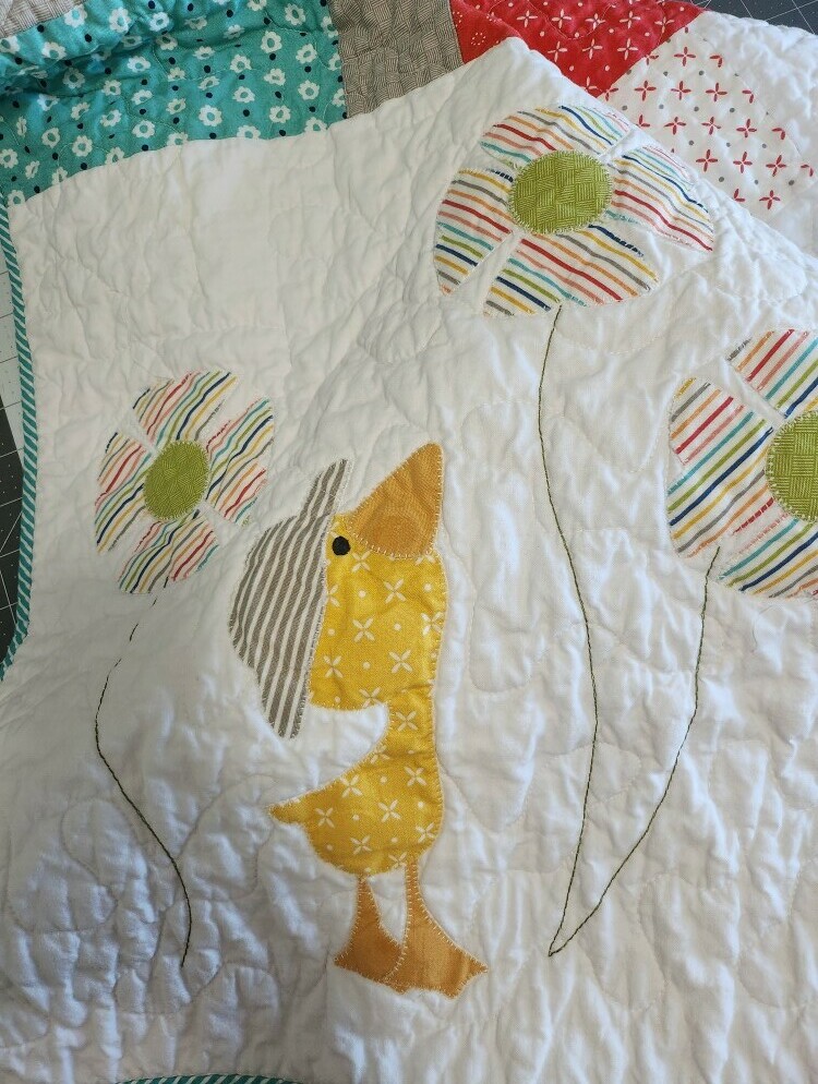 Yellow fabric duck applique on quilt with free motion quilted white background