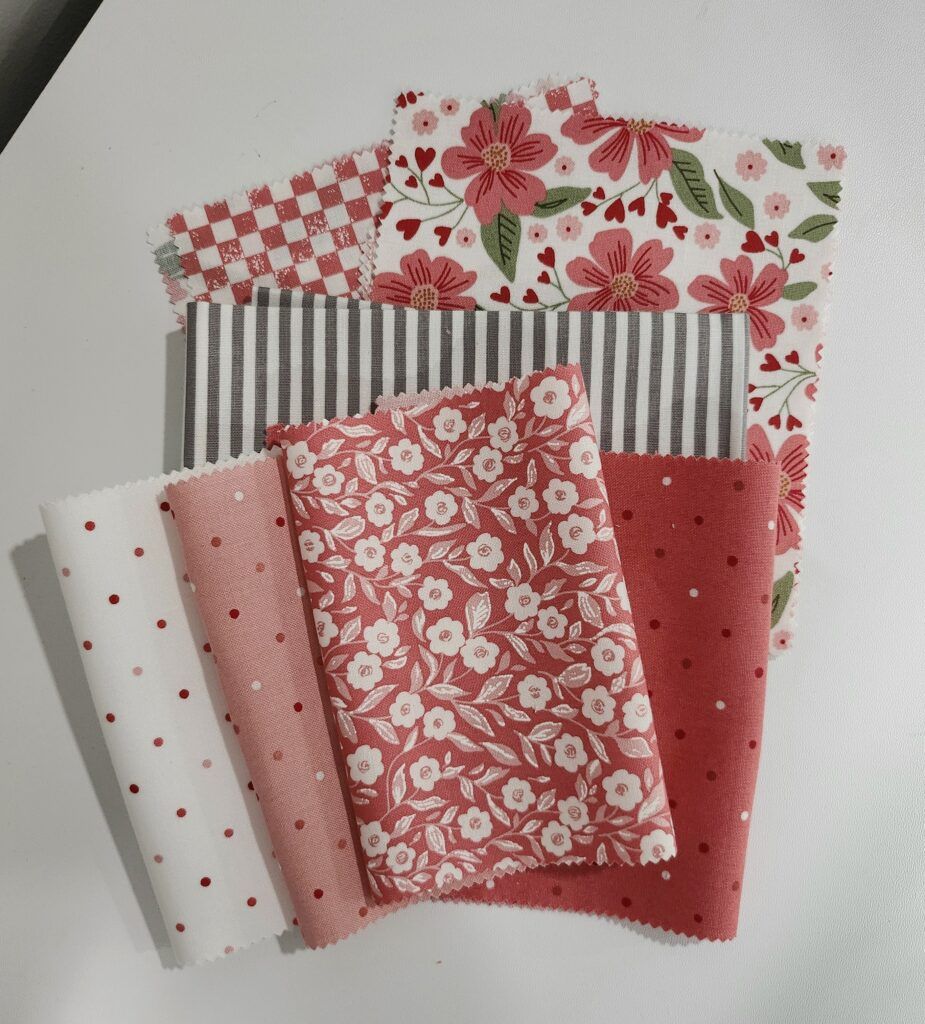 Loosely stacked fabrics in a variety of pink, red, white, green and gray dots, florals and stripes.