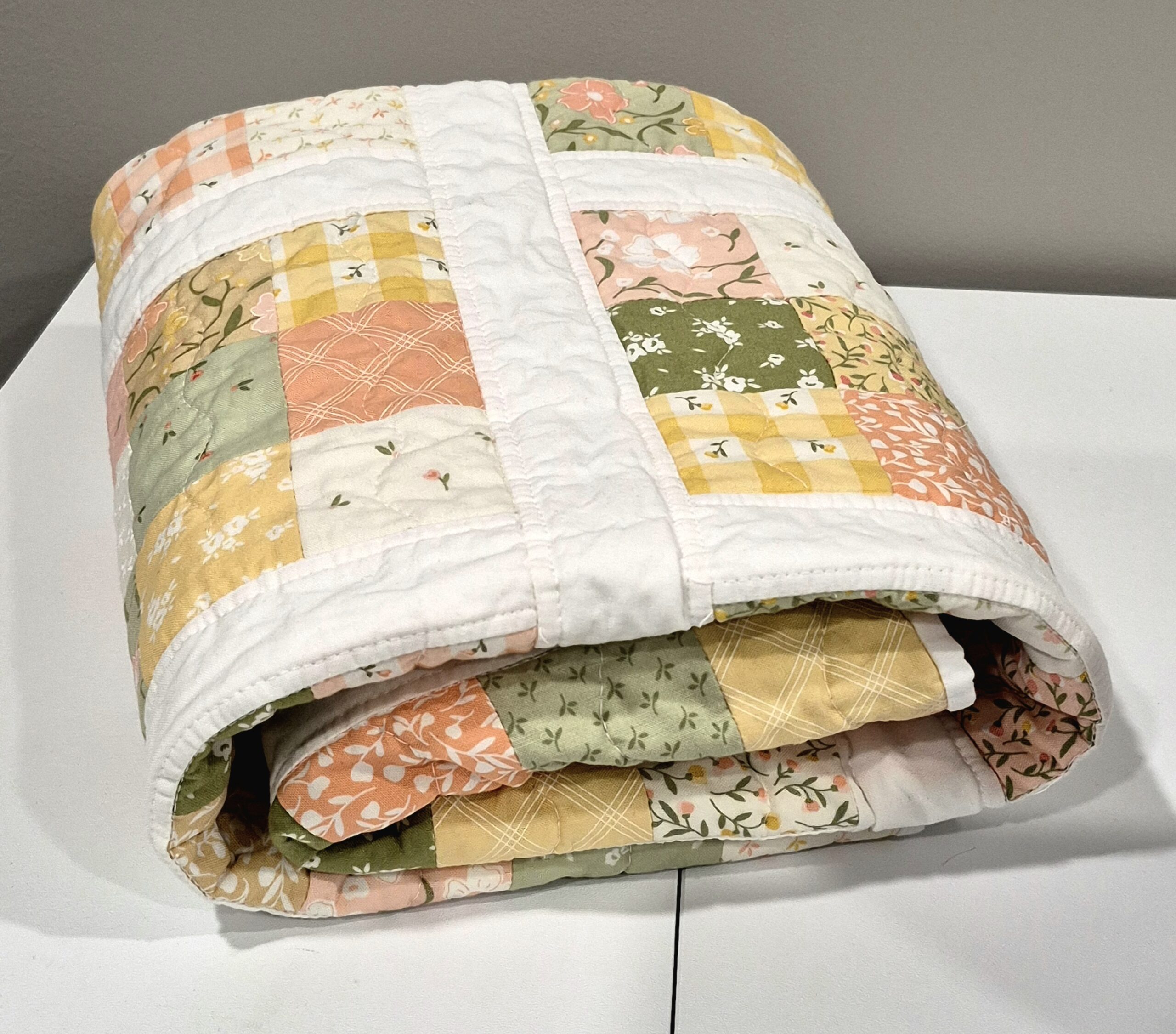 Folded patchwork quilt using Flower Girl fabrics in shades of pink, yellow and green.