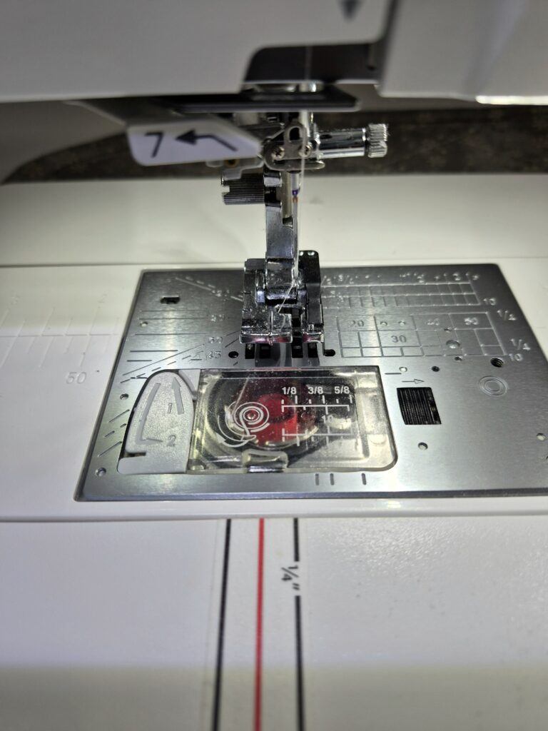 Footbed of sewing machine showing use of a 1/4" presser foot and washi tape used as guides for a perfect seam allowance.